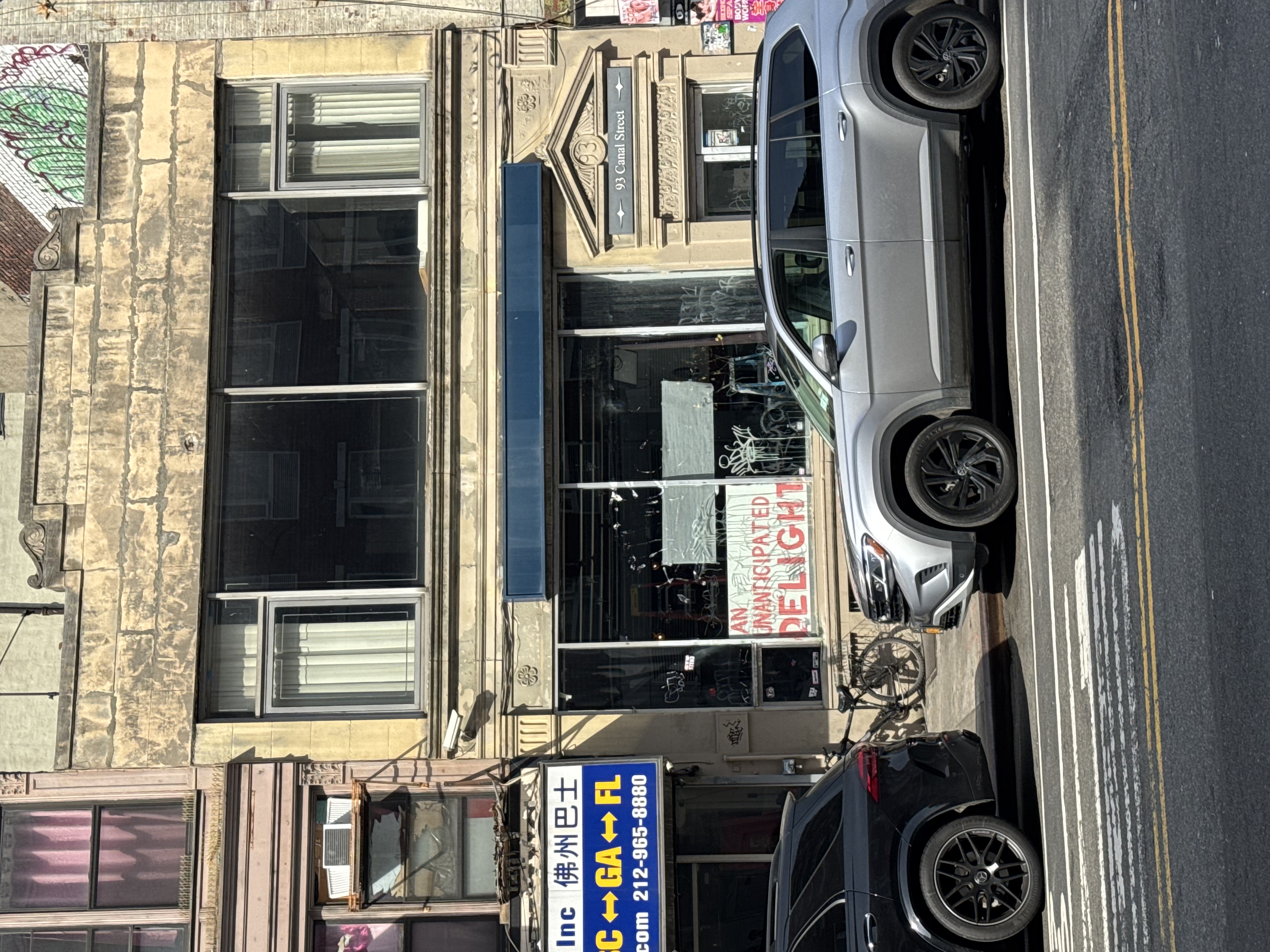 Photo of 93 Canal facade in NYC, white sign with handpainted letters in window reads AN UNANTICIPATED DELIGHT